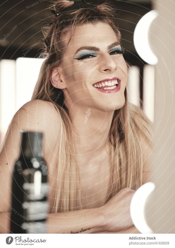 Fröhlicher androgyner Mann mit Make-up, der lacht Lachen Stil stydio Spiegel Transgender Glück Atelier jung männlich Model lange Haare queer lgbtq Drag Queen