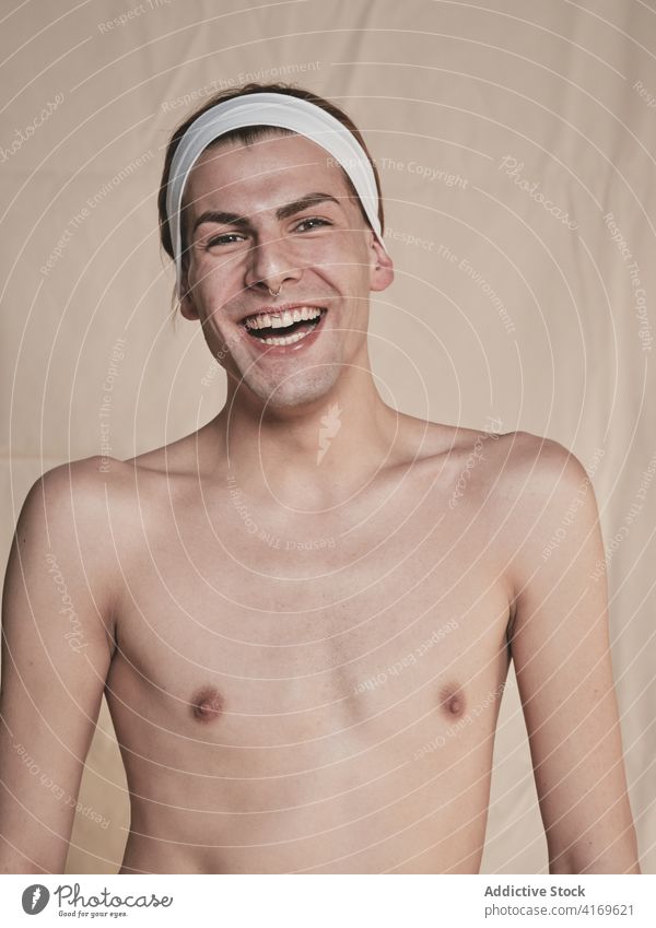 Junger hemdloser androgyner Mann lachend Lachen Make-up ohne Hemd Vorschein Transgender Glück Model jung männlich Stirnband Piercing aufgeregt queer lgbtq