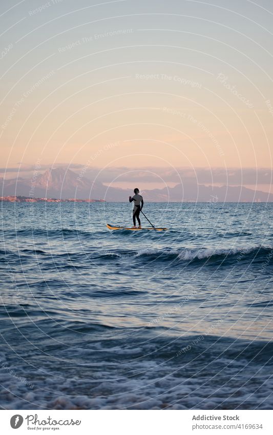 Mann im Neoprenanzug auf Paddleboard im Meer Paddelbrett Surfer Reihe Brandung SUP MEER Training männlich Sommer Sport Wasser Sonnenuntergang Natur genießen