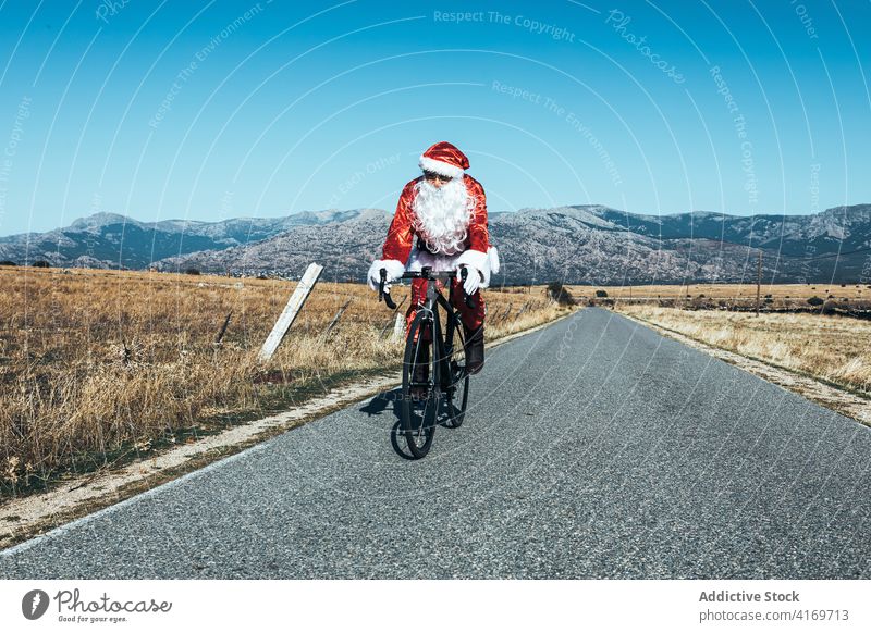 Weihnachtsmann auf dem Fahrrad entlang der Bergstraße Mitfahrgelegenheit Straße leer Berge u. Gebirge Tracht rot Farbe männlich modern Reise Freiheit