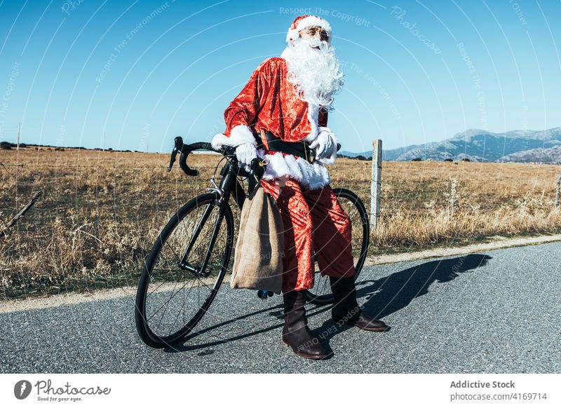 Weihnachtsmann in der Nähe von Fahrrad auf der Straße auf dem Lande Landschaft Tasche sich[Akk] entspannen Fahrbahn Fahrzeug Weihnachtsmütze männlich Vollbart