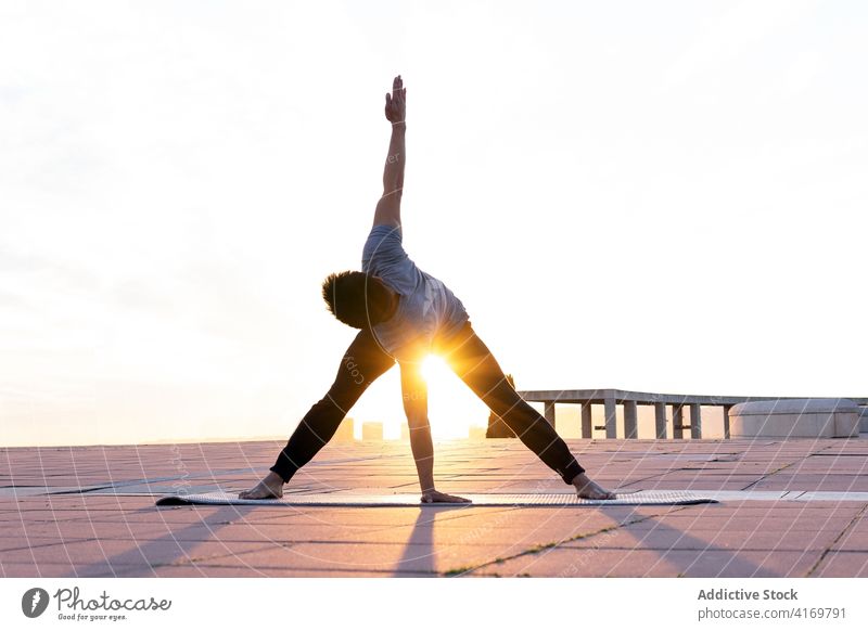 Flexibler Mann übt Yoga in einer gedrehten, breitbeinigen Vorwärtsbeuge beweglich Asana gedrehte weitbeinige Vorwärtsbeuge-Pose Gleichgewicht Sonnenuntergang
