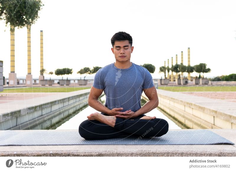 Gelassener Mann in Lotus-Pose im Park vermittelnd meditieren Yoga Harmonie Asana padmasana beweglich Beine gekreuzt üben männlich ethnisch asiatisch Unterlage