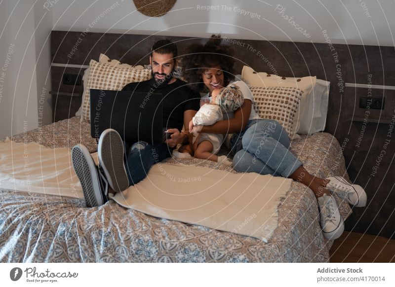 Multiethnische Familie benutzt gemeinsam einen Laptop auf dem Bett zuschauen Karikatur Baby Zusammensein Vater heimwärts sich[Akk] entspannen bezaubernd weich