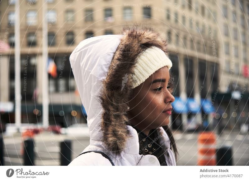 Verträumte ethnische Frau in warmer Jacke in der Stadt Großstadt schlendern verträumt sorgenfrei Straße Spaziergang warme Kleidung Saison schwarz Afroamerikaner