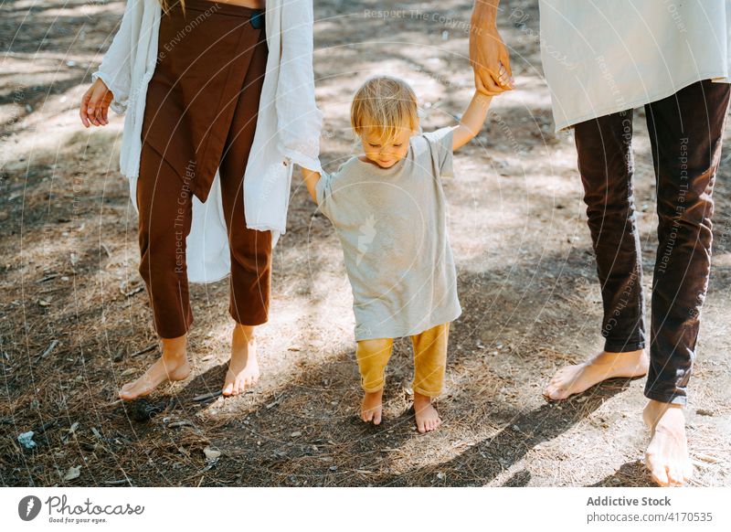 Anonymes Paar beim Spaziergang mit Kind im Wald Hippie Familie Barfuß Natur genießen Einheit multiethnisch rassenübergreifend vielfältig Wälder sonnig niedlich