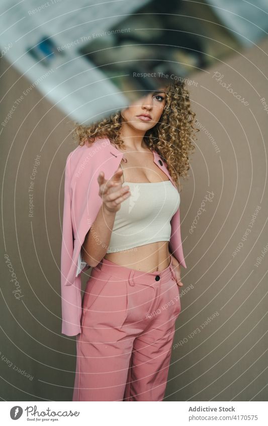 Nachdenkliche Frau in stilvollem Outfit im Studio besinnlich Anzug Tracht rosa Afro-Look Frisur trendy lange Haare modern stehen ernst Denken traumhaft charmant