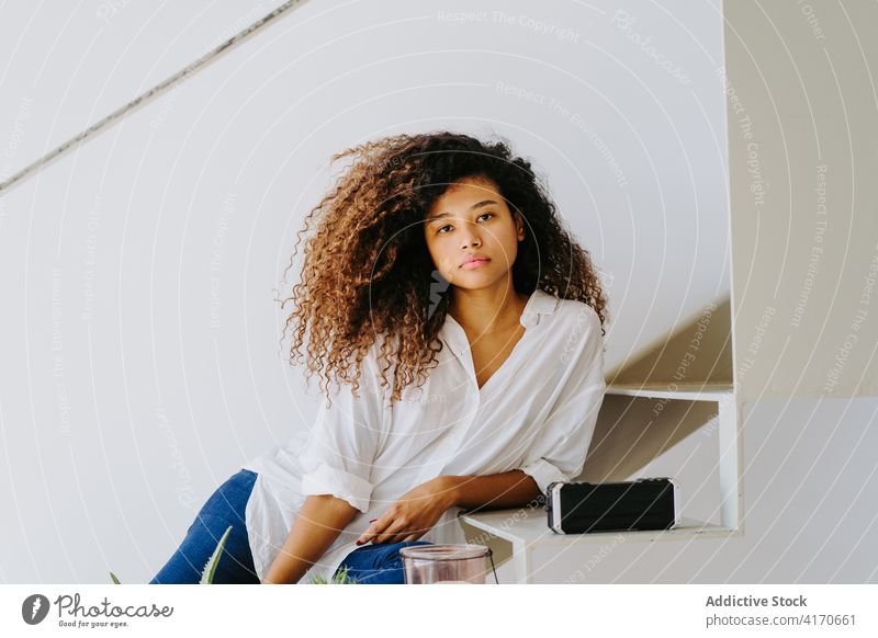 Stilvolle ethnische Frau mit lockigem Haar sitzt auf Stufen zu Hause krause Haare Afro-Look trendy Treppe Windstille sich[Akk] entspannen modern attraktiv jung