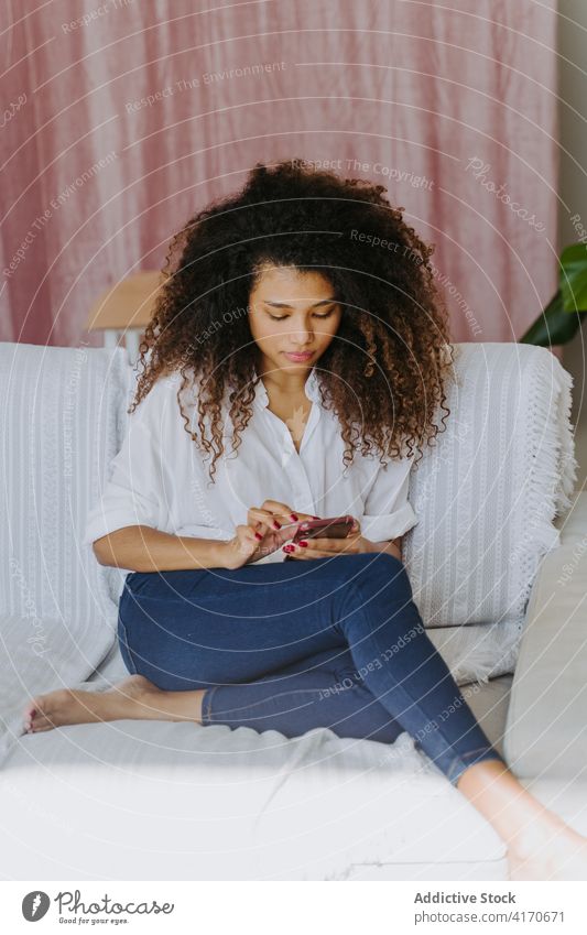 Ethnische Frau surft auf dem Sofa auf ihrem Smartphone zu Hause Browsen benutzend Internet Mobile Telefon Apparatur jung Afroamerikaner schwarz lässig Gerät