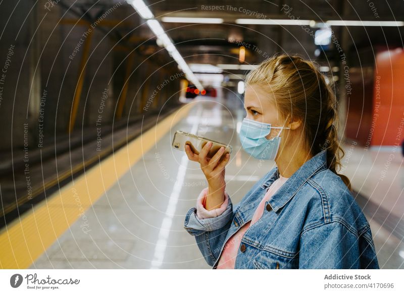 Maskierte Frau nimmt am Bahnhof eine Sprachnachricht auf ihrem Smartphone auf Passagier benutzend Funktelefon Coronavirus Nachricht Stimme Eisenbahn Station