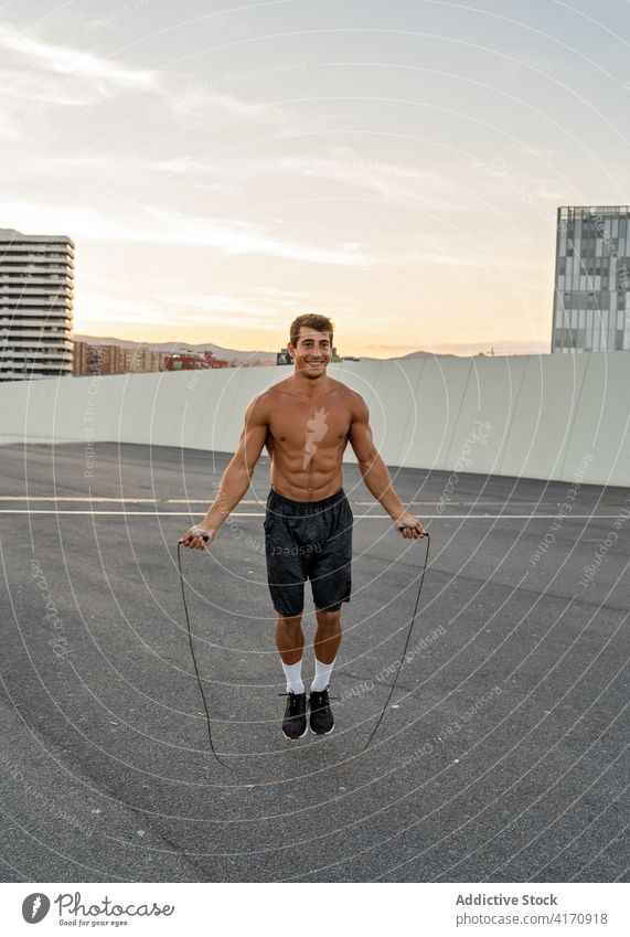 Glücklicher Sportler beim Seilspringen auf der Straße in der Dämmerung Athlet Hüpfseil Herz Training Übung Lächeln Großstadt Mann Inhalt muskulös ohne Hemd