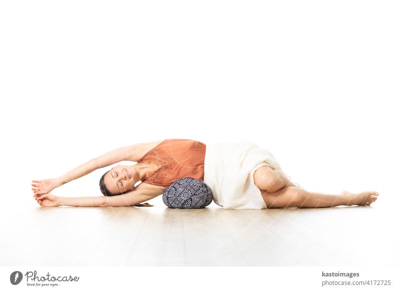 Restorative Yoga mit einem Bolster. Junge sportliche attraktive Frau in hellen weißen Yoga-Studio, auf Kissen liegend, Stretching und Entspannung während Restorative Yoga. Gesunder aktiver Lebensstil
