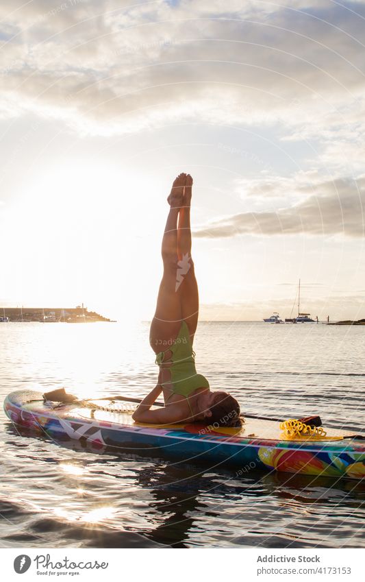 Frau übt ausgleichende Yoga-Pose auf dem Paddelbrett Holzplatte salamba sarvangasana Umkehrung Gleichgewicht Asana MEER Sonnenuntergang Zusatzplatine