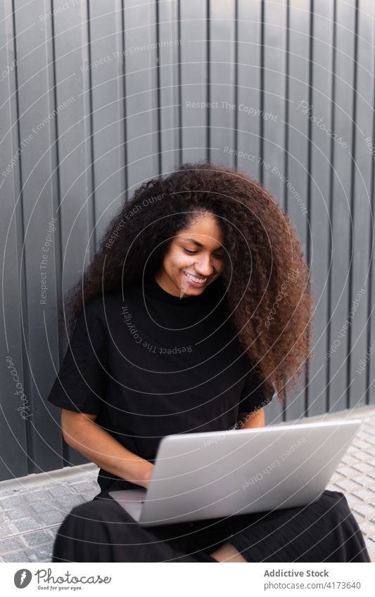 Fröhliche afroamerikanische selbständige Frau mit Laptop auf der Straße sitzend freiberuflich krause Haare Großstadt Unternehmer ethnisch schwarz Afroamerikaner