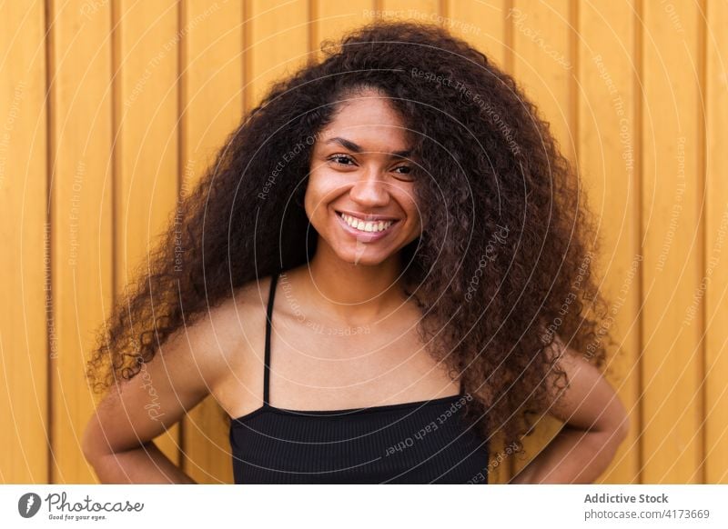 Fröhliche schwarze Frau mit lockigem Haar auf der Straße krause Haare Afro-Look Frisur Lächeln Porträt herzlich offen jung ethnisch Afroamerikaner Freude