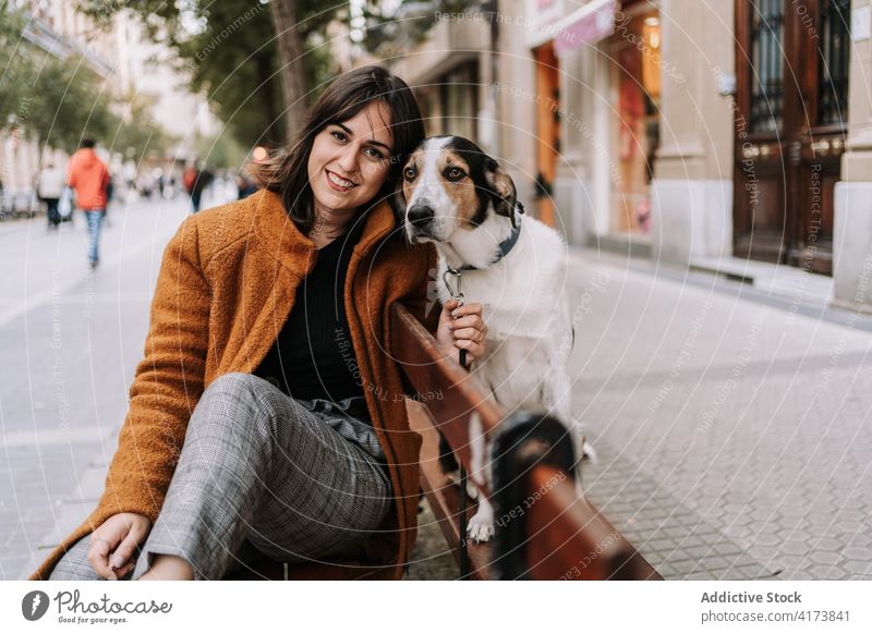 Lächelnde Frau mit liebenswertem Hund auf der Straße freundlich Großstadt Bank Haustier Tier schlendern heiter hölzern Glück Eckzahn sitzen Freund heimisch