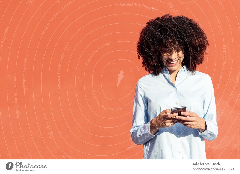 Lächelnde ethnische Geschäftsfrau beim Surfen mit dem Handy auf der Straße Frau Großstadt Smartphone Unternehmer formal Hemd modern Apparatur Gerät krause Haare