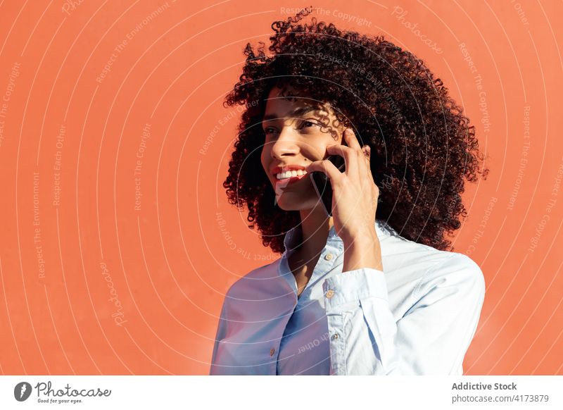 Lächelnde ethnische Geschäftsfrau spricht auf Handy ion der Straße Frau Großstadt Smartphone Unternehmer formal Hemd modern Apparatur Gerät krause Haare Inhalt