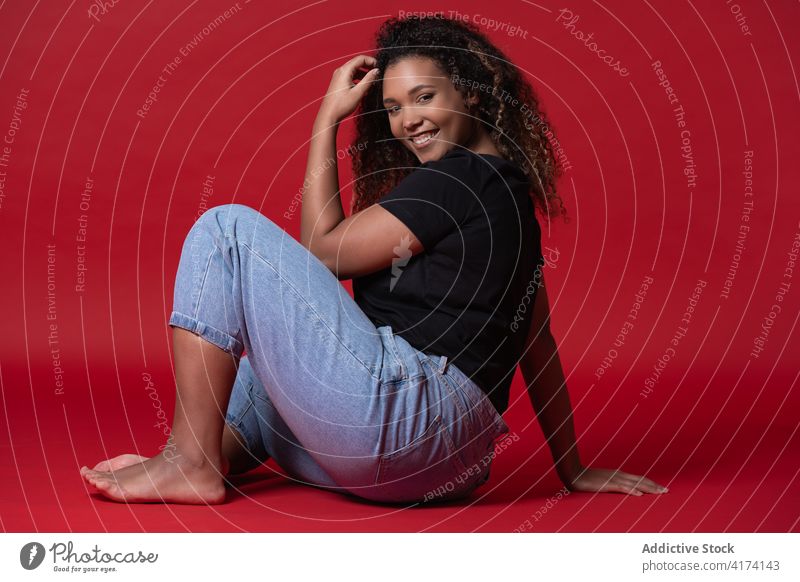 Fröhliches weibliches Modell in Übergröße in lässigem Outfit Frau Übergewicht Jeanshose Glück heiter Stil Lächeln jung Afroamerikaner schwarz ethnisch Barfuß