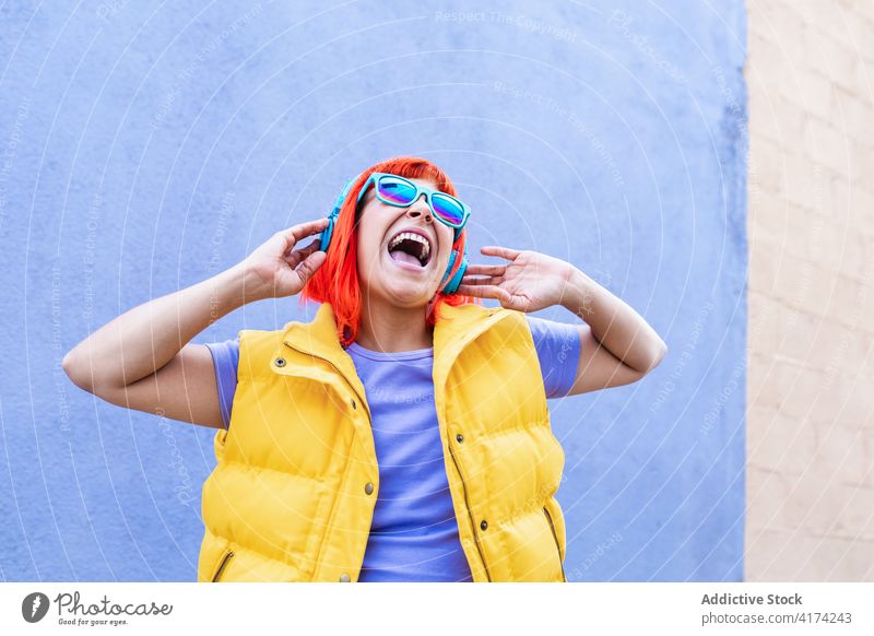 Aufgeregte rothaarige Frau beim Hören von Musik zuhören Zeichen Glück Straße Großstadt auflehnen farbenfroh hell Erwachsener tausendjährig laut schreien