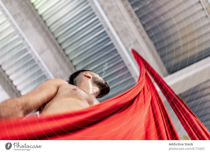 Hemdloser männlicher Tänzer mit rotem Tuch Mann Gewebe packen Probe Atelier Seide ohne Hemd Turner üben Erwachsener Bändchen Stoff Zimmerdecke Choreographie