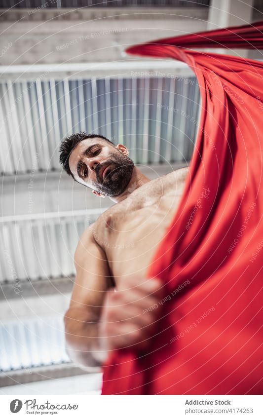 Hemdloser männlicher Tänzer mit rotem Tuch Mann Gewebe packen Probe Atelier Seide ohne Hemd Turner üben Erwachsener Bändchen Stoff Zimmerdecke Choreographie