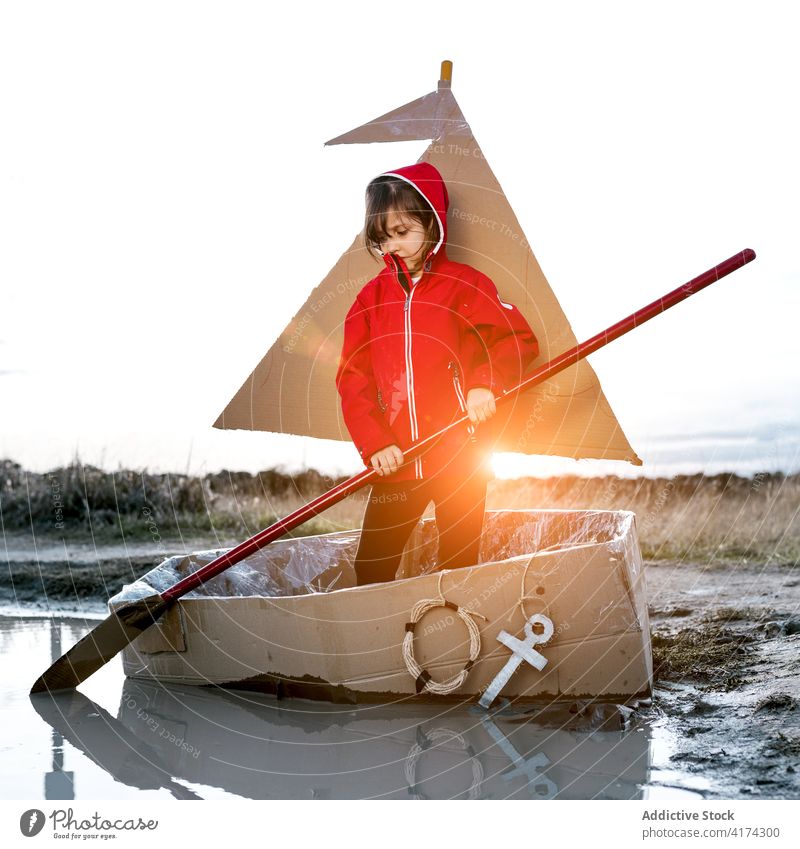 Verspieltes Mädchen in Kartonboot auf dem Lande Schachtel Boot Zusammensein Paddel Spaß haben Reihe Kind spielen Inspiration Spiel kreativ Vorstellungskraft
