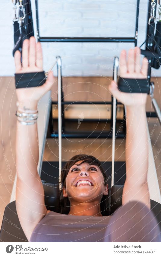 Glückliche Frau, die ihre Arme auf dem Pilates-Reformer dehnt Übung Fitnessstudio Lächeln Dehnung Arme hochgezogen Widerstandsband Training Erwachsener
