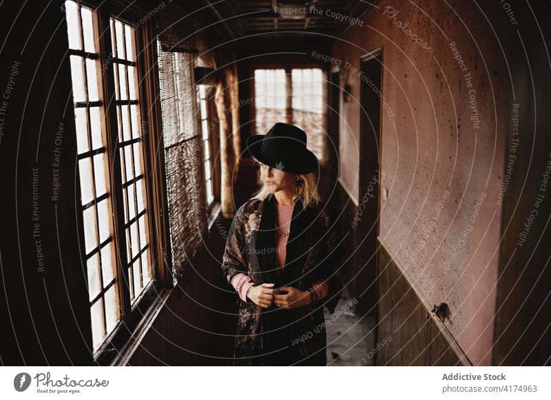 Frau mit Hut im Korridor eines alten Hauses stehend altehrwürdig Fenster Gang Stil altmodisch elegant Flur retro besinnlich nachdenklich Verlassen Kunst