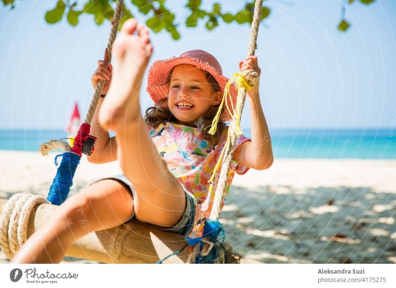 Glückliche niedliche kleine Mädchen lachen und schwingen auf Schaukel auf dem Baum am Strand. Schöne Sommer sonnigen Tag, türkisfarbenes Meer, Felsen, weißer Sand, malerische tropische Landschaft. Phuket, Thailand. Unbeschwert