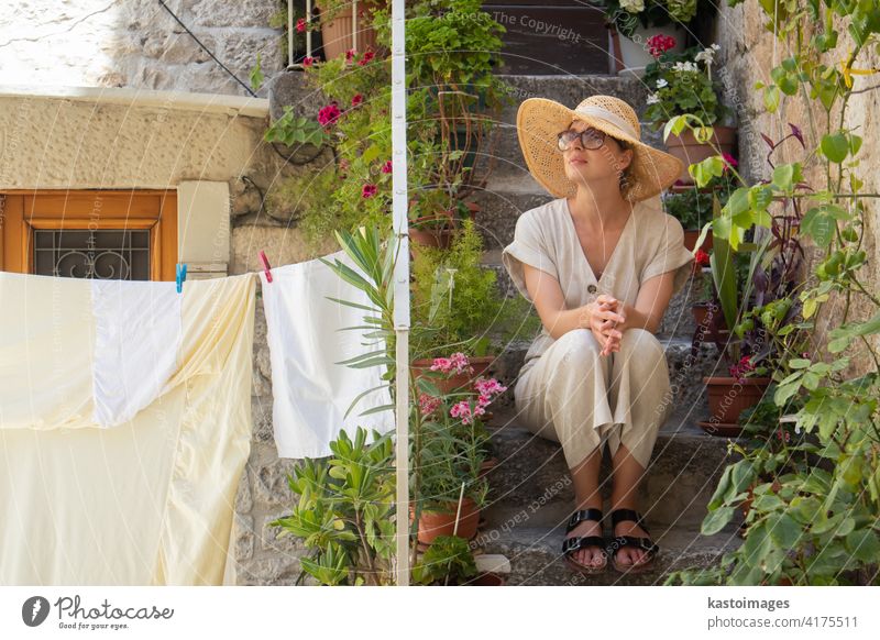 Schöne weibliche Touristin trägt große Strohsonnenhut und sundress sitzen und entspannen auf alten Stein Haus Treppen während der Sommerreise auf Mittelmeer-Küste auf heißen Sommertag