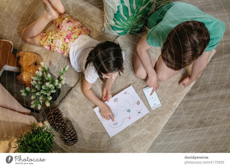 Unbekannte Kinder spielen Schatzsuche zu Hause auf dem Teppich Draufsicht unkenntlich Schatzsuchspiel mobiler Kompass Landkarte Blick zu Hause bleiben