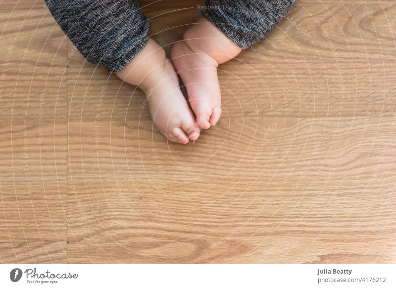 Kleinkind auf Laminatboden sitzend; die Füße berühren sich, während sich die Beine in einer offenen Sitzhaltung ausbreiten, ähnlich der Schmetterlingspose im Yoga