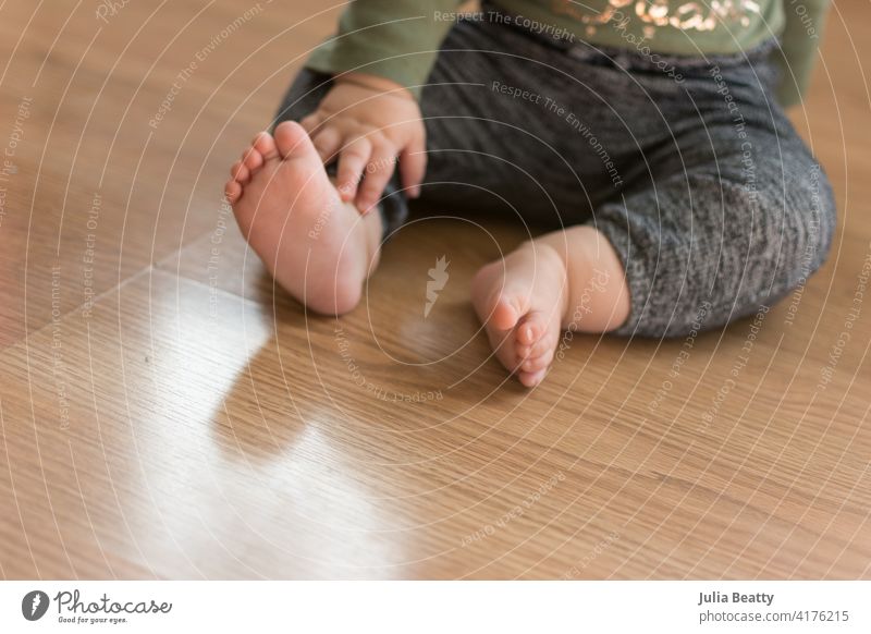 Kleinkind Baby sitzt auf Laminat Holzboden mit nackten Füßen; über zu krabbeln weg Treffen einer Entwicklungs Meilenstein unabhängig Kilometerstein