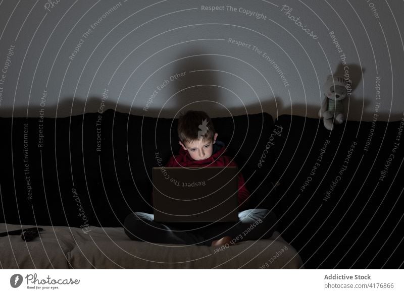 Junge mit Laptop auf dem Sofa liegend zu Hause benutzend besinnlich Kind Browsen Internet Apparatur Gerät online Freizeit Surfen männlich Anschluss abgelegen