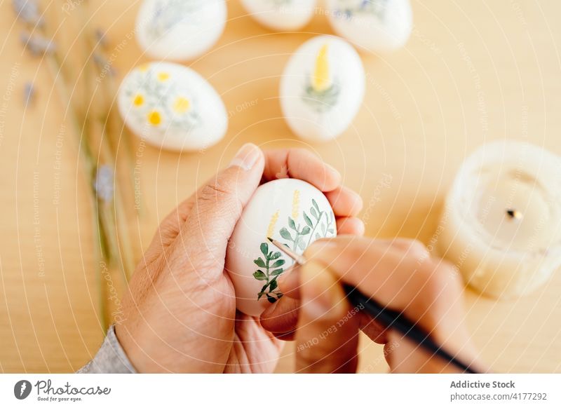 Crop Artist bemalt Eier für Ostern Anstreicher Farbe religiös Feiertag vorbereiten Kunstwerk Blume Frühling Aquarell Lebensmittel Tradition Tisch Religion Dekor