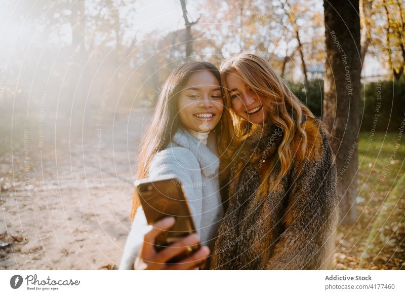 Freundliche Frauen machen ein Selfie im Herbstpark Smartphone heiter Selbstportrait Gedächtnis Park schlendern rassenübergreifend multiethnisch vielfältig Foto