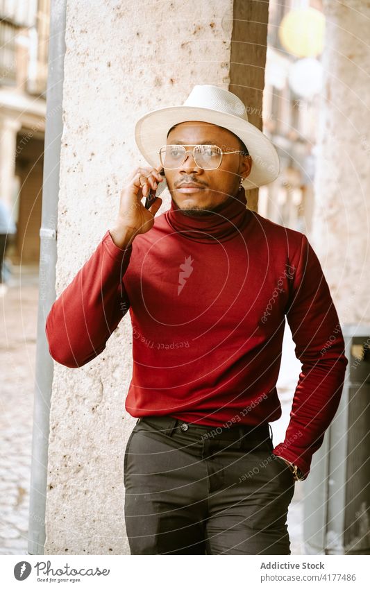 Schwarzer Mann in stilvollem Outfit spricht in der Stadt mit seinem Smartphone elegant reden Stil Großstadt Straße Bestimmen Sie trendy Hut männlich ethnisch