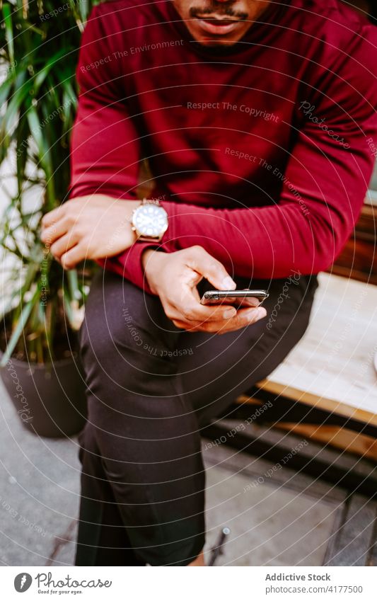 Anonymer schwarzer Mann durchsucht Smartphone in der Nähe eines Cafés in der Stadt Browsen Großstadt Surfen soziale Netzwerke Straße Stil trendy männlich