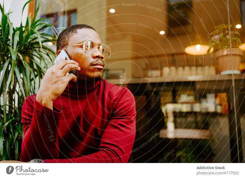 Schwarzer Mann spricht in der Nähe eines Cafés in der Stadt mit seinem Smartphone Browsen Großstadt Surfen soziale Netzwerke Straße Stil trendy männlich