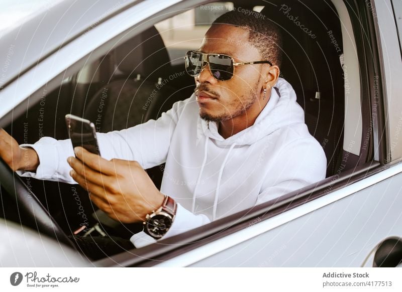 Stilvoller schwarzer Mann benutzt Smartphone in Luxusauto PKW Browsen Reichtum schick Bestimmen Sie Surfen Internet Fahrer männlich ethnisch Afroamerikaner