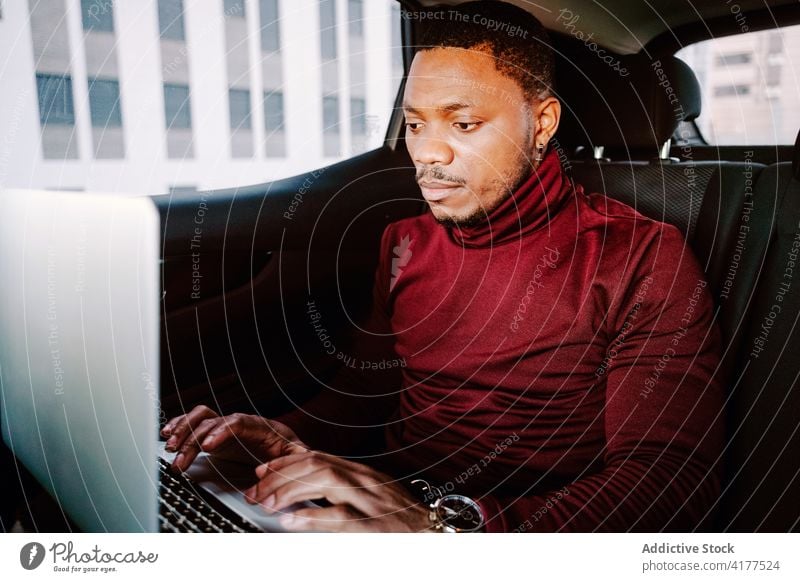 Seriöser schwarzer Geschäftsmann tippt auf Laptop im Auto Arbeit PKW Projekt Mann Unternehmer beschäftigt Tippen Automobil männlich Afroamerikaner ethnisch