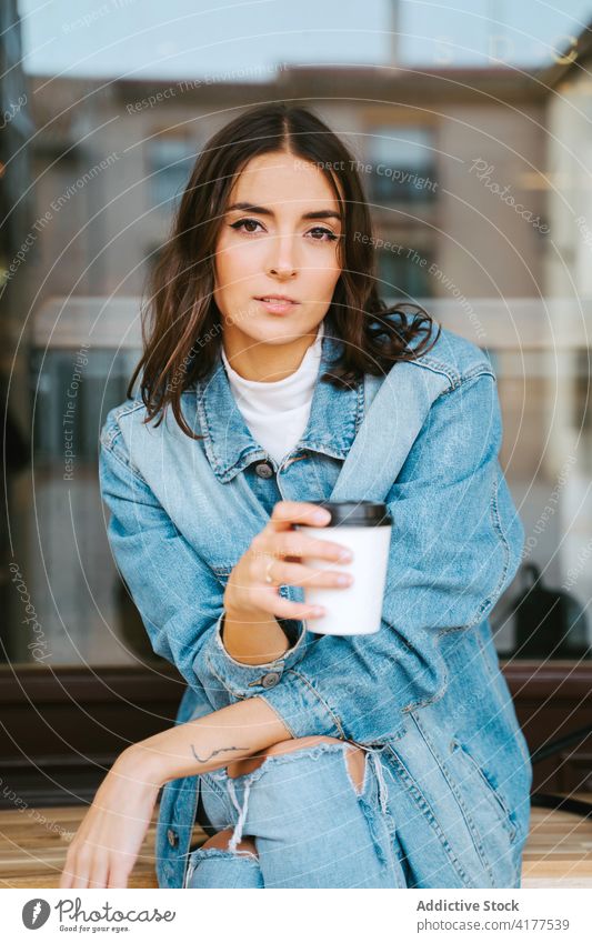 Junge Frau mit Kaffee zum Mitnehmen, die sich auf der Straße ausruht ruhen Imbissbude trinken Tasse Jeansstoff modern sich[Akk] entspannen urban Windstille jung