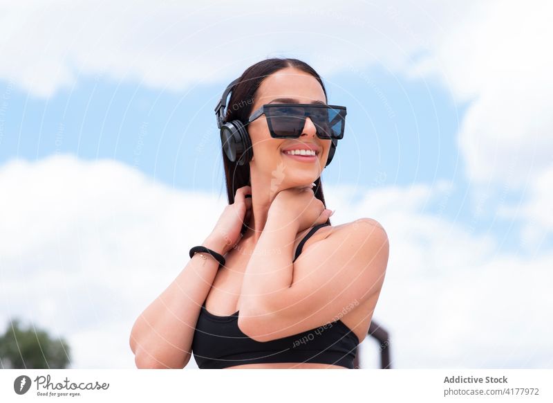Trendy fit Frau mit Kopfhörer und Sonnenbrille passen trendy Stil positiv heiter sportlich Glück jung Drahtlos zuhören Musik Mode Lifestyle Lächeln Optimist