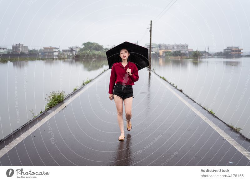 Frau zu Fuß entlang nassen Straße am regnerischen Tag Regen Spaziergang Regenschirm wolkig Asphalt allein Einsamkeit schlendern Kreis Yilan Taiwan leer bedeckt