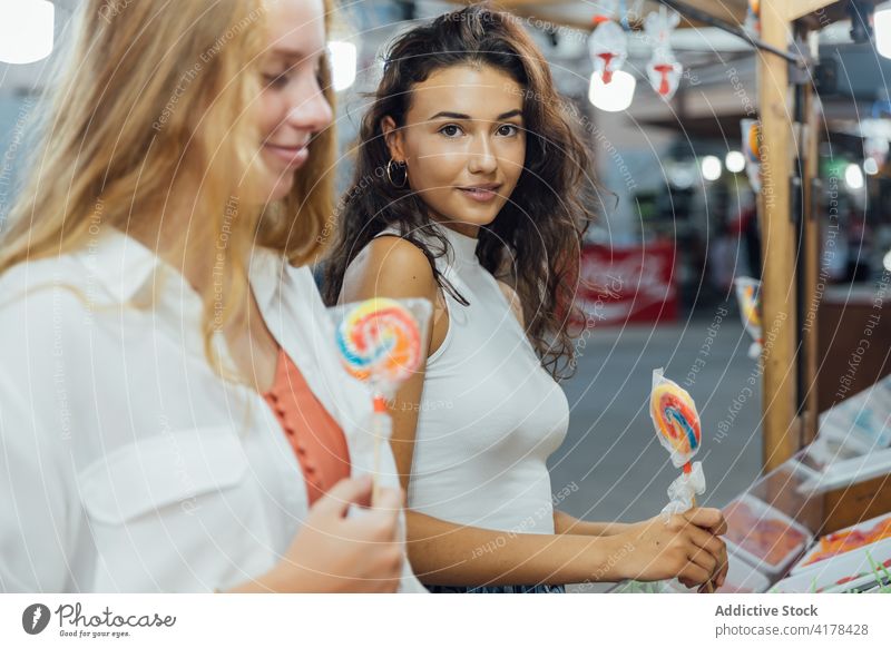 Glückliche Freundinnen mit Lutschern auf dem Rummelplatz Lollipop Jahrmarkt Sommer jung Bonbon Messegelände genießen Feiertag Frauen Teenager Zusammensein