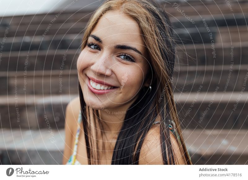 Fröhliche junge Frau, die sich auf einer Treppe in der Stadt ausruht heiter Lächeln positiv Glück modern urban Porträt lange Haare brünett gefärbtes Haar