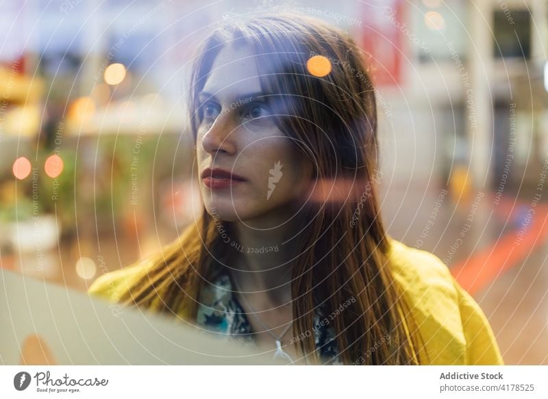 Nachdenkliche junge Frau, die durch ein Glasschaufenster schaut positiv Fenster urban Vitrine modern Optimist Werkstatt Straße Lifestyle Menschliches Gesicht