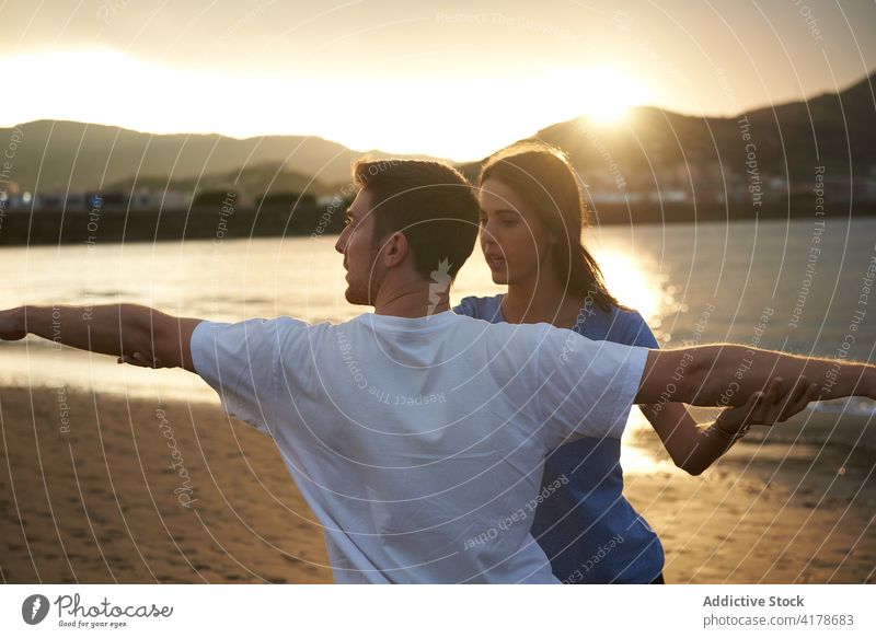 Mann macht Yoga in Kriegerhaltung mit Hilfe eines Lehrers üben Ausbilderin abstützen Gesundheit Hilfsbereitschaft Krieger-Pose MEER Strand Sonnenuntergang Frau