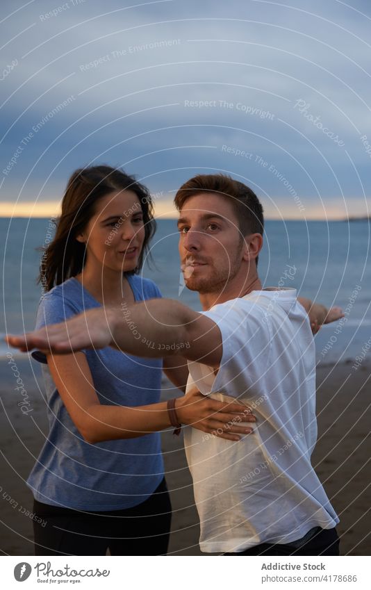 Mann macht Yoga in Kriegerhaltung mit Hilfe eines Lehrers üben Ausbilderin abstützen Gesundheit Hilfsbereitschaft Krieger-Pose MEER Strand Sonnenuntergang Frau